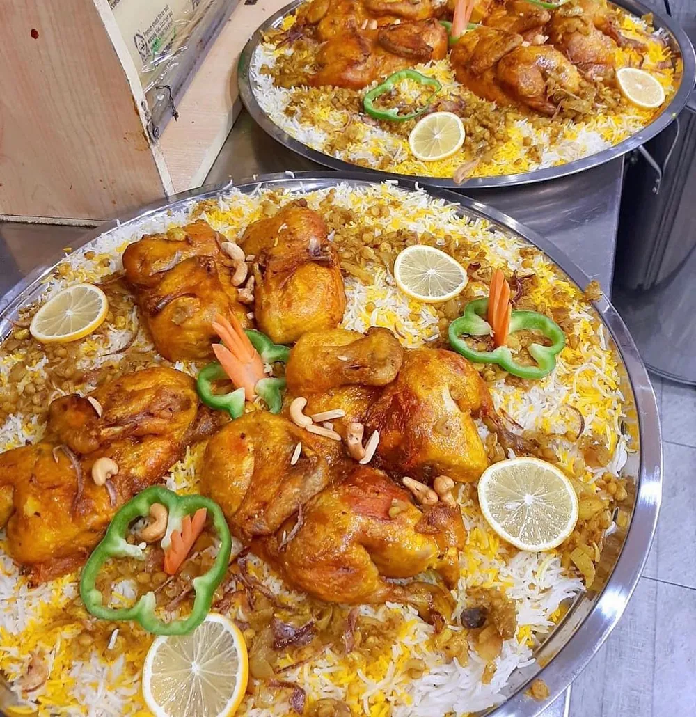 Two steel platters of golden rice topped with roasted chicken, cashews, lemon slices and green pepper rings