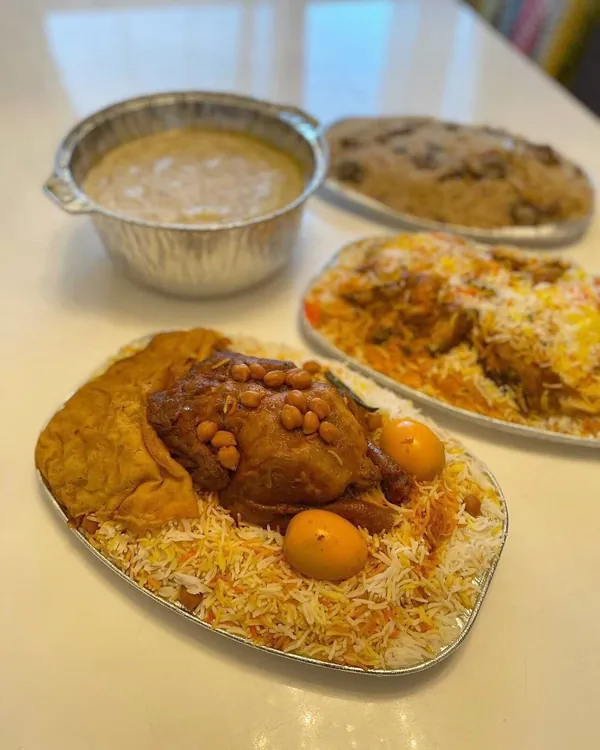 Takeaway foil trays of rice with chicken, chickpeas and whole eggs, beside a bowl of creamy porridge