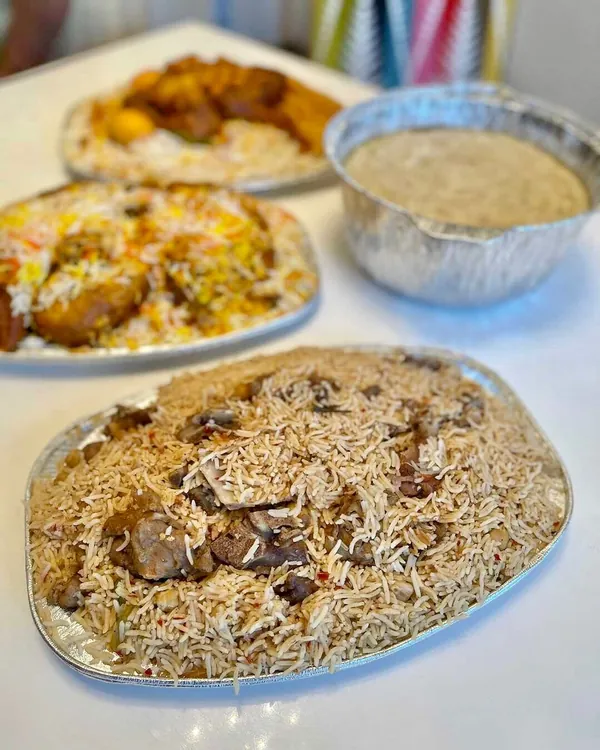 Takeaway foil trays of spiced rice with meat beside a bowl of creamy porridge